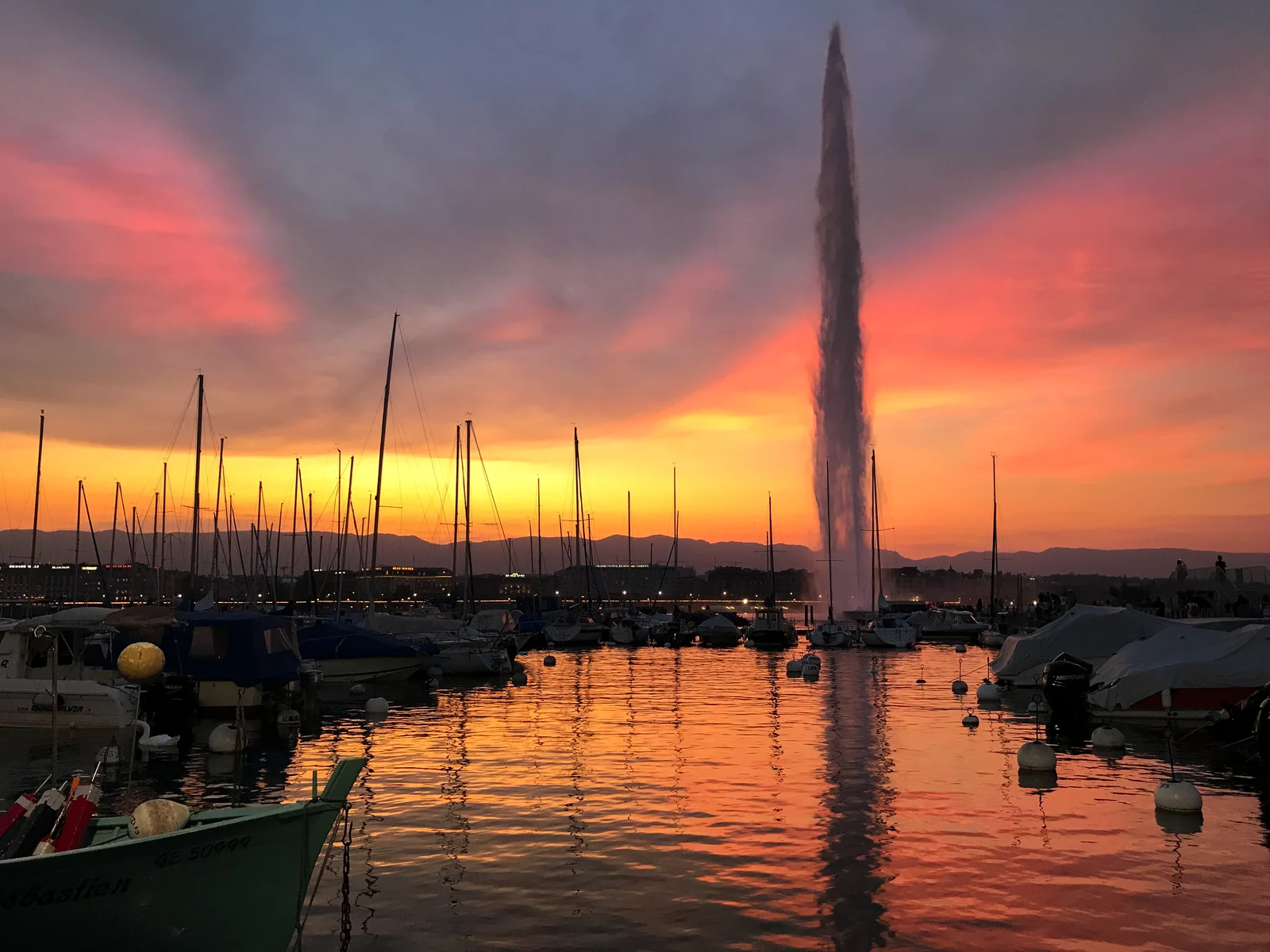 Le Jet d'eau de Genève et les bateaux du port des Eaux-Vives au coucher du soleil.
